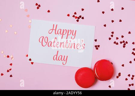 Valentinstag Komposition mit Grußkarte mit Text, zwei Macarons und herzförmige Konfetti auf rosa Hintergrund Stockfoto