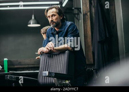 Schöner Mann in Jeans Kleidung stehend mit Schere und Suchen Stockfoto