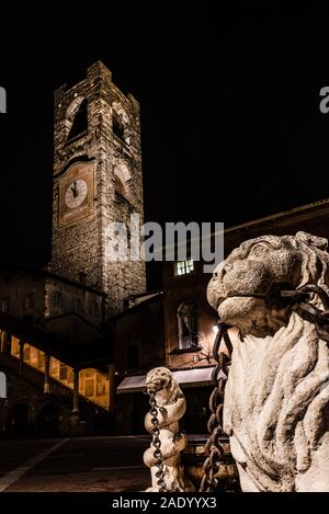 Nahaufnahme der Löwe der Contarini Brunnen mit im Hintergrund der Campanone der Città Alta in Piazza Vecchia Bergamo, vertikale Nacht Bild Stockfoto