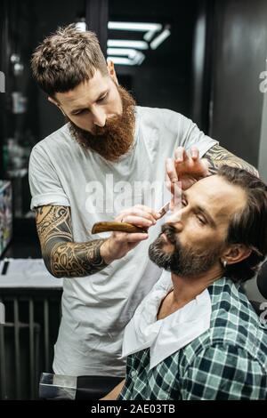 In der Nähe von schweren Friseur holding Rasiermesser und Rasieren sein Klient Stockfoto