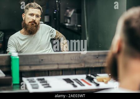 Tätowierten Mann sitzt und auf sein Spiegelbild im Spiegel Stockfoto
