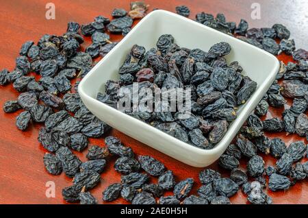 Schwarze Rosinen in eine Schüssel geben und auf einen hölzernen Tisch. Stockfoto