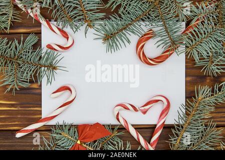 Auf einer hölzernen Hintergrund weiß Blatt Papier umgeben von Zweigniederlassungen von Blue Spruce und Weihnachten Süßigkeiten. Stockfoto