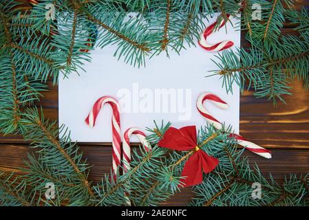 Auf einer hölzernen Hintergrund weiß Blatt Papier umgeben von Zweigniederlassungen von Blue Spruce und Weihnachten Süßigkeiten. Stockfoto