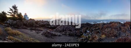 Schöne Panoramasicht auf die felsigen Pazifik Küste während einer farbenfrohen Sonnenaufgang mit dem Leuchtturm im Hintergrund. Auf Wild Pacific Trail genommen Stockfoto