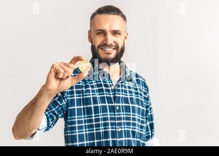 Freestyle. Kerl in kariertem Hemd stehen auf weißen Anzeigen cryptocurrency Münze schließen isoliert, verschwommenen Hintergrund lächelt Fröhlich Stockfoto