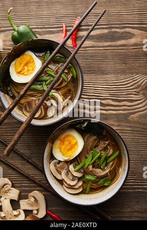 Blick von oben auf die traditionellen würzige Ramen in Schalen mit Stäbchen und Gemüse auf hölzernen Tisch Stockfoto