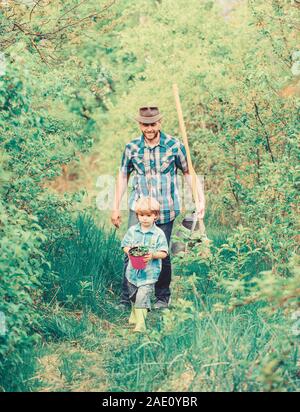 Kleine Helfer im Garten. Blumen Pflanzen. Wachsende Pflanzen. Sohn und Vater in der Natur mit Gießkanne und Schaufel. Vati lehre Sohn pflege Pflanzen. Arbor Day. Die Anpflanzung von Bäumen. Baumpflanzung Tradition. Stockfoto