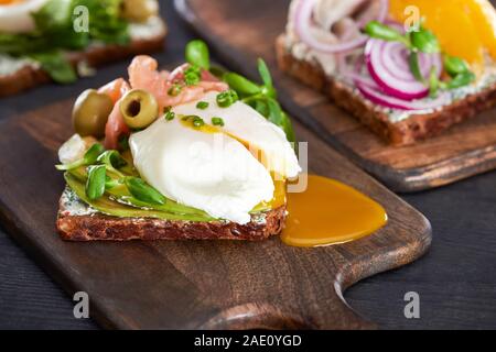 Nahaufnahme der leckeren smorrebrod Sandwich mit pochiertem Ei in der Nähe von frischem Lachs auf Holz Schneidebrett Stockfoto