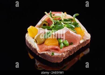 Selektiver Fokus der Schinken und Oliven auf gekochte Dänische smorrebrod Sandwich auf Schwarz Stockfoto