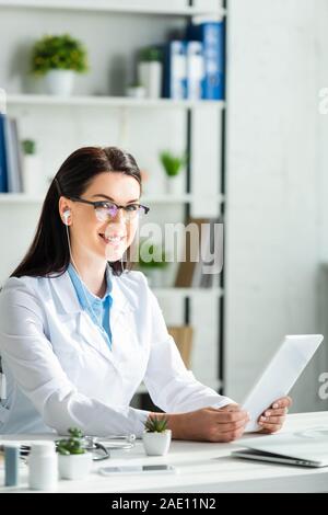 Positive Arzt in Online-Konsultation zu digitalen Tablet in Klinik Büro mit Laptop Stockfoto