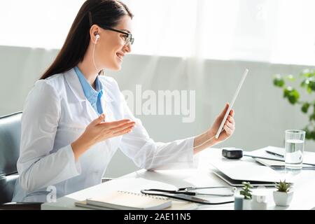 Lächelnd Arzt in Online-Konsultation zu digitalen Tablet in Klinik Büro mit Laptop Stockfoto