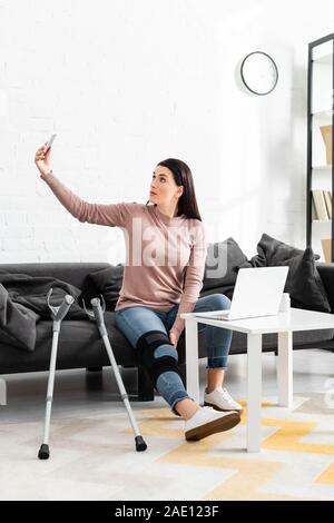 Frau mit gebrochenen Bein in On-line-Konsultation mit dem Arzt auf Laptop und Smartphone Stockfoto