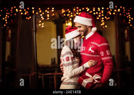 Glückliches Paar in warme Pullover und santa Hüte, die auf der Straße Stockfoto