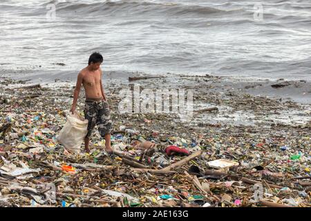 Manila, Philippinen - 23. August 2017: ein Mann sammeln von Kunststoffabfällen in einem Haufen Müll im Meer Stockfoto