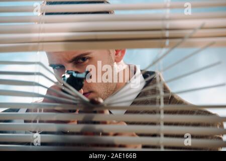 Selektiver Fokus gefährlicher Gangster holding Gun in der Nähe von Jalousien Stockfoto