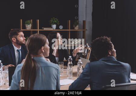 Junge Geschäftsfrau Sprechen während der Konferenz beim Sitzen in der Nähe von multikulturellen Kollegen Stockfoto