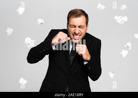 Stattlich und Angst Geschäftsmann im Anzug in der Nähe von sinkenden zerknittertes Papier isoliert auf Grau Stockfoto
