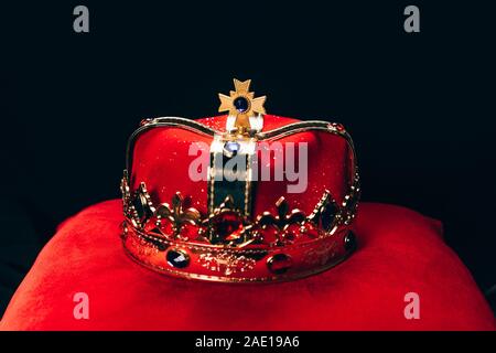 Alte goldene Krone mit Edelsteinen auf dem roten Kissen, isoliert auf Schwarz Stockfoto