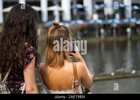 Zwei junge Frauen, die ein Bild mit Ihrem Handy der Alsterarkaden in Hamburg an einem sonnigen Sommertag Stockfoto