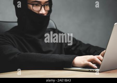 Selektiver Fokus der asiatische Hacker mit mit Laptop und Sitzen am Tisch verdeckt Gesicht Stockfoto