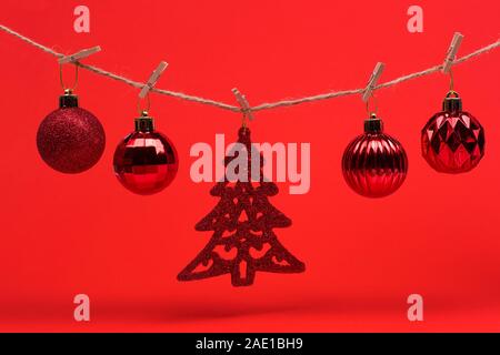Neues Jahr Weihnachten Hintergrund. Rot Weihnachten Spielzeug Bälle auf einem String mit Wäscheklammern auf einem roten Hintergrund, Vorbereitung für das Neue Jahr und Weihnachten. Stockfoto