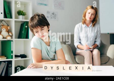 Selektiver Fokus der traurige Kinder mit Legasthenie am Tisch sitzen mit Holzwürfeln mit Schriftzug Legasthenie Stockfoto