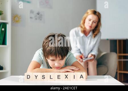 Selektiver Fokus der traurige Kinder mit Legasthenie am Tisch sitzen mit Holzwürfeln mit Schriftzug Legasthenie Stockfoto