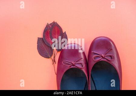 Stilvolle weibliche flache Schuhe in dunkelrote Farbe und Herbstlaub auf orange Farbe Papier Hintergrund mit Copyspace. Herbst Fashion Kollektion Konzept. Stockfoto