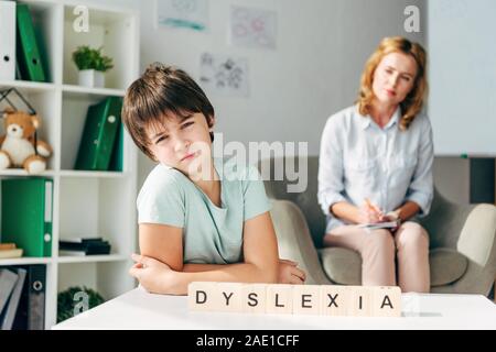 Selektiver Fokus der traurige Kinder mit Legasthenie am Tisch sitzen mit Holzwürfeln mit Schriftzug Legasthenie Stockfoto
