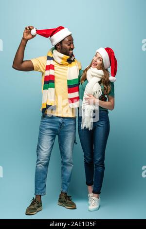 Happy interracial Paare in santa Hüte und Schals auf blauem Hintergrund Stockfoto