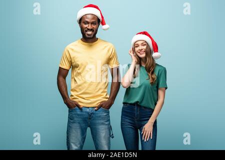 Lächelnd interracial Paare in santa Hüte auf blauem Hintergrund Stockfoto