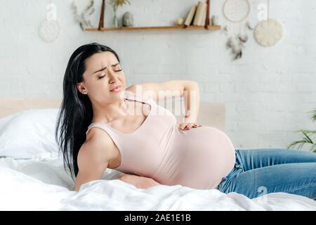 Schwangere Frau in Schmerzen und berühren Bauch auf dem Bett besorgt Stockfoto