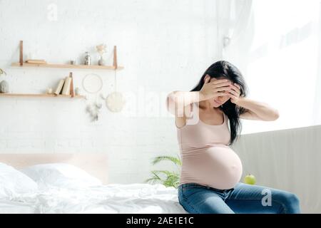 Schöne schwangere Frau in Kopfschmerzen im Schlafzimmer Stockfoto