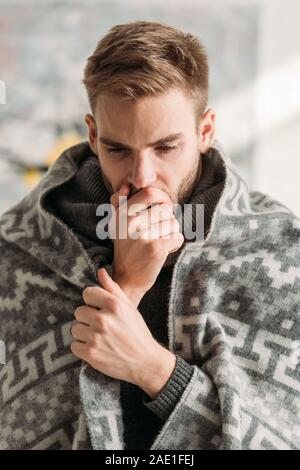 Kranken Mann, in der Decke eingewickelt, Husten und deckt den Mund mit der Hand Stockfoto