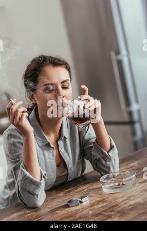 Frau rauchen Zigaretten und Whiskey Glas am Tisch Stockfoto