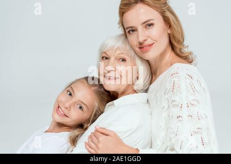Lächelnd Enkelin, Mutter und Großmutter umarmt isoliert auf Grau Stockfoto
