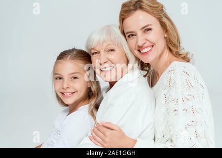 Lächelnd Enkelin, Mutter und Großmutter umarmt isoliert auf Grau Stockfoto