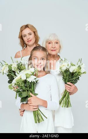 Lächelnd Enkelin, Mutter und Großmutter halten Blumensträuße isoliert auf Grau Stockfoto