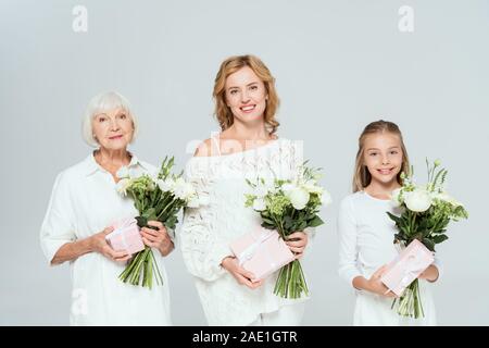 Lächelnd Enkelin, Mutter und Großmutter holding Sträuße und Geschenke isoliert auf Grau Stockfoto