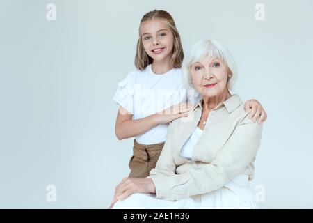 Lächelnd und süße Enkelin umarmen Großmutter isoliert auf Grau Stockfoto