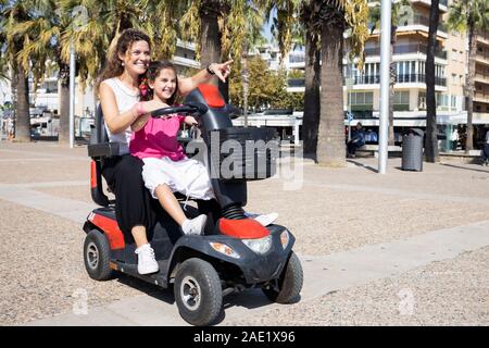 Mutter und Tochter auf einem elektrischen Stuhl, der auf der Straße Stockfoto