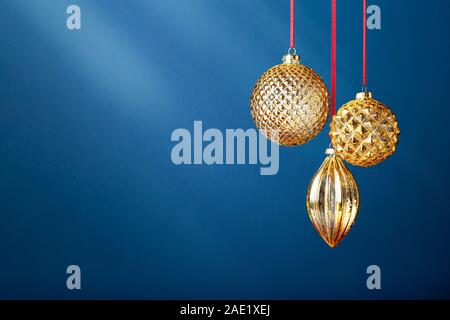Drei goldene Weihnachtskugeln hängen an den klassischen blauen Hintergrund. Neues Jahr Grußkarte. Stockfoto