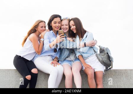 Happy charmante Schüler Mädchen sitzen, mit Smartphone und lächelnd im Park auf dem Hintergrund der Himmel Stockfoto