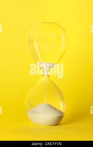 Die Zeit läuft. Eine Sanduhr mit Sand Tropfen durch, der auf einer lebhaften gelben Hintergrund Stockfoto