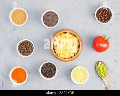 Pasta, Tomaten, grüne Zwiebeln, Masala, roter Chili, Nelken, Piment, Käse, Senf Samen auf grauem Beton Hintergrund. Gesunde Ernährung Konzept Stockfoto