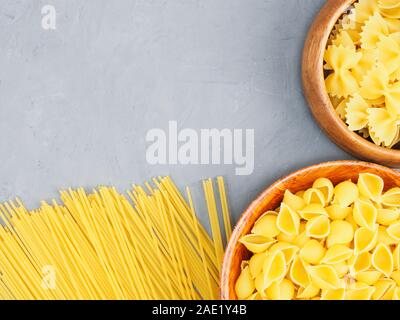 Verschiedene Arten von Nudeln in hölzernen Schüsseln und auf grauem Beton Hintergrund mit kopieren. Gesunde Ernährung Konzept Stockfoto