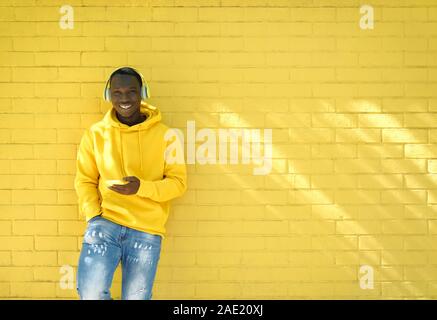 Afrikanische jungen Mann Musik hören lehnte sich auf gelbe Wand Stockfoto