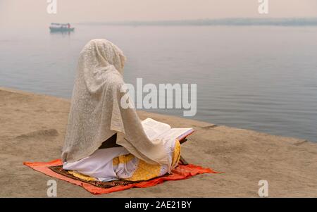 Einsame Hinduistische Frau in Schal tief in der Mediation am Ufer des Flusses Yamuna im Morgengrauen in Vrindavan, Uttar Pradesh, Indien. Stockfoto