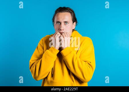 Europäischen Mann Angst vor etwas Angst und sieht in die Kamera mit großen Augen voller Entsetzen über blaue Wand Hintergrund. Stockfoto
